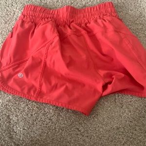 lululemon tracker 4 inch shorts in warm coral which is a pinkish red color